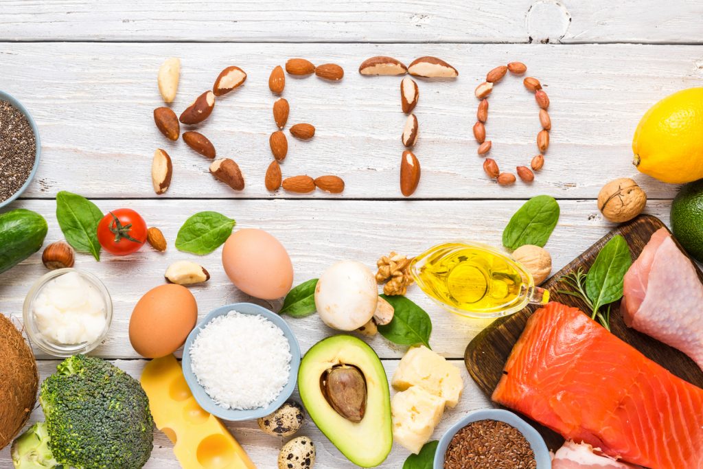 Almond halves arranged to spell "keto" surrounded by low-carb foods including eggs, salmon, and cheese