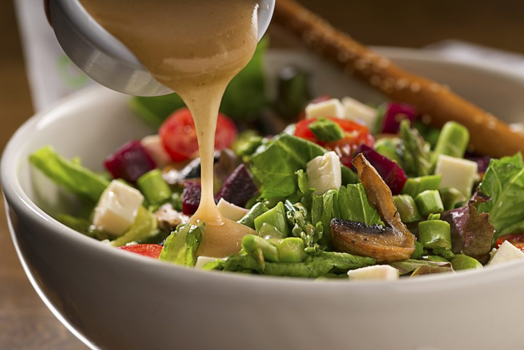 A salad with a small container of dressing being poured over the top.