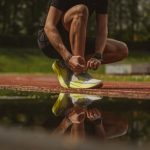 A man crouching near a puddle to tie his running shoes