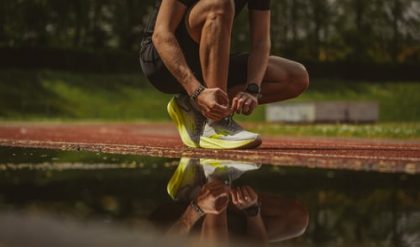 A man crouching near a puddle to tie his running shoes