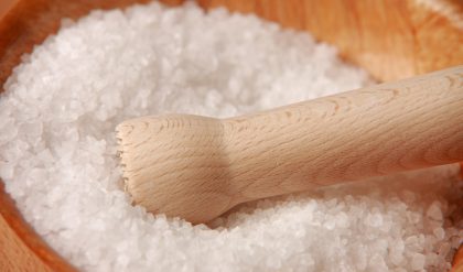 A wooden mortar and pestle filled with white salt.