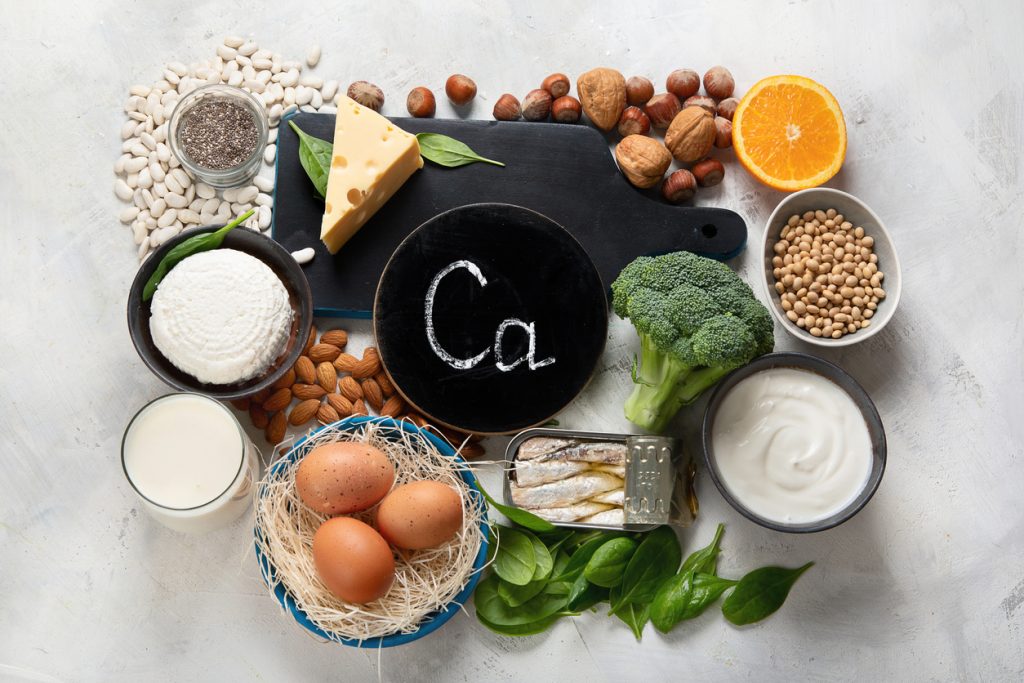 An array of calcium-rich foods surrounding a chalkboard circle with Ca written on it in white chalk.