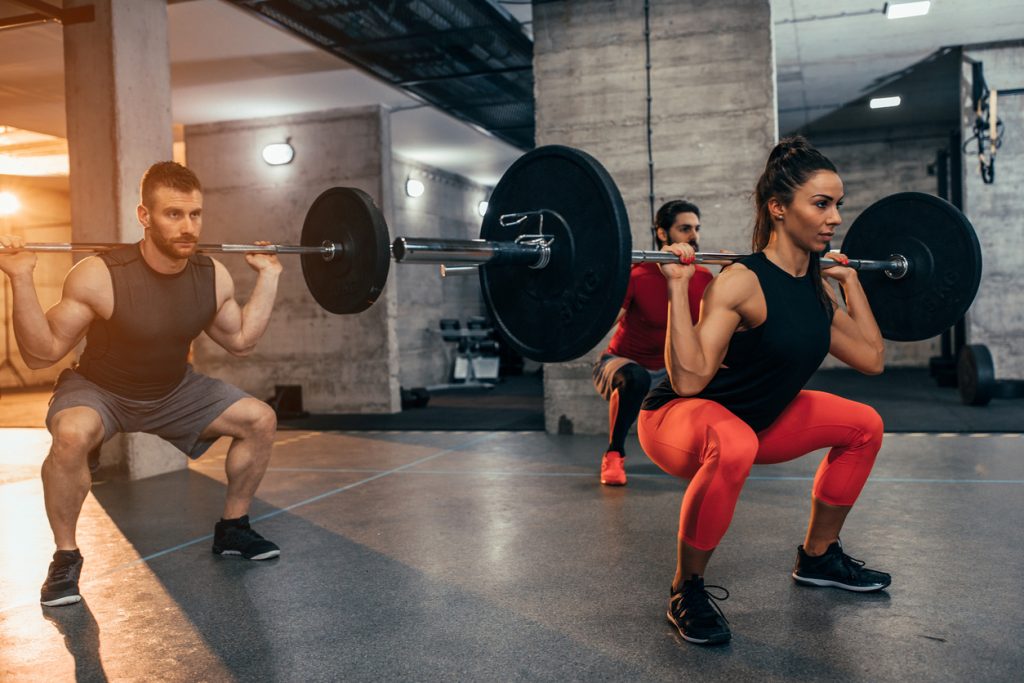A man and a woman squatting with weights in a gym room.