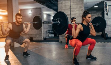 A man and a woman squatting with weights in a gym room.